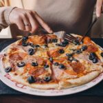 Fetta di pizza con ingredienti freschi e colorati su un piatto, simbolo di convivialità e piacere occasionale.