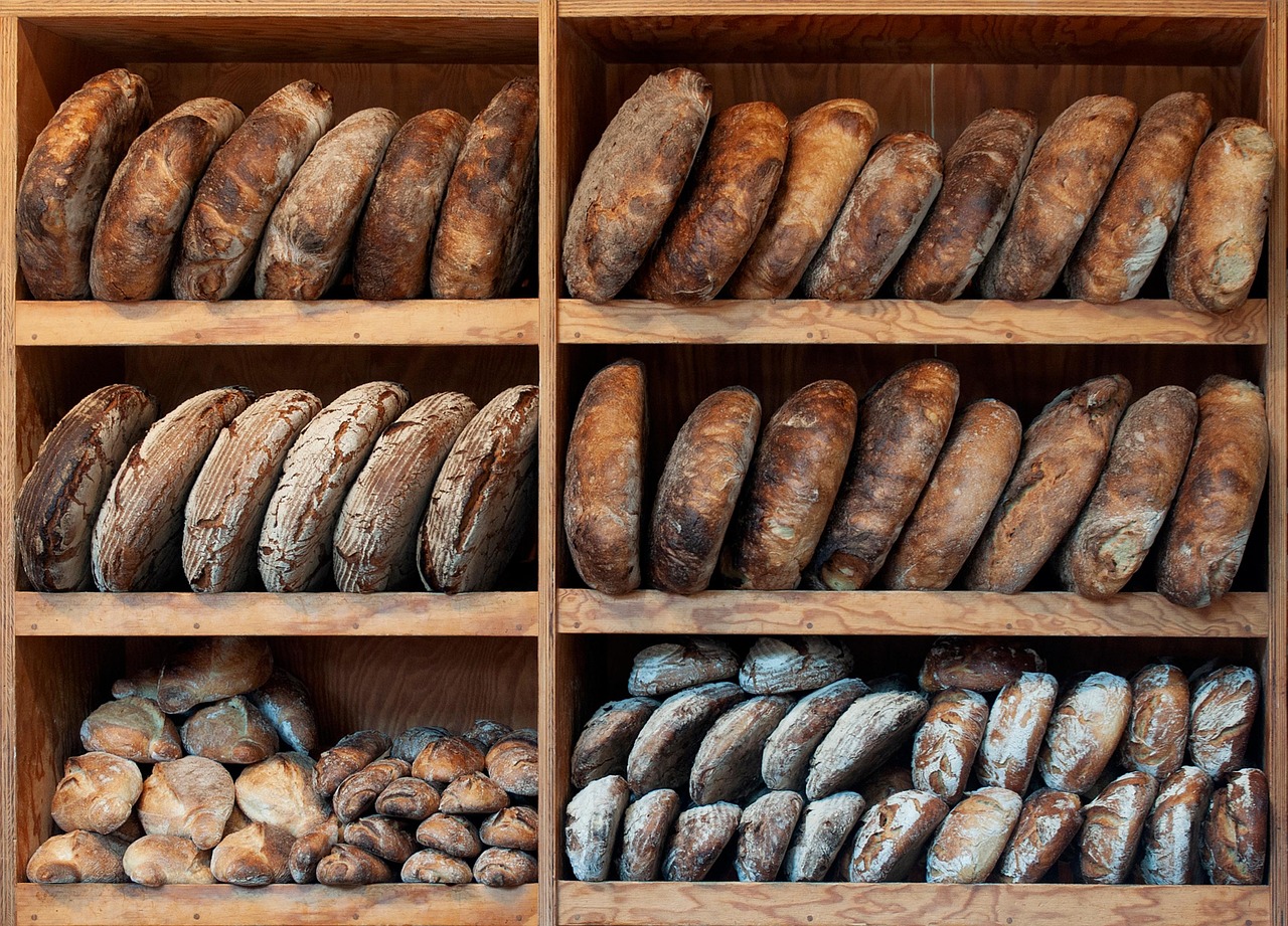 Pane fresco appena sfornato su un tagliere, circondato da ingredienti per conservarlo.